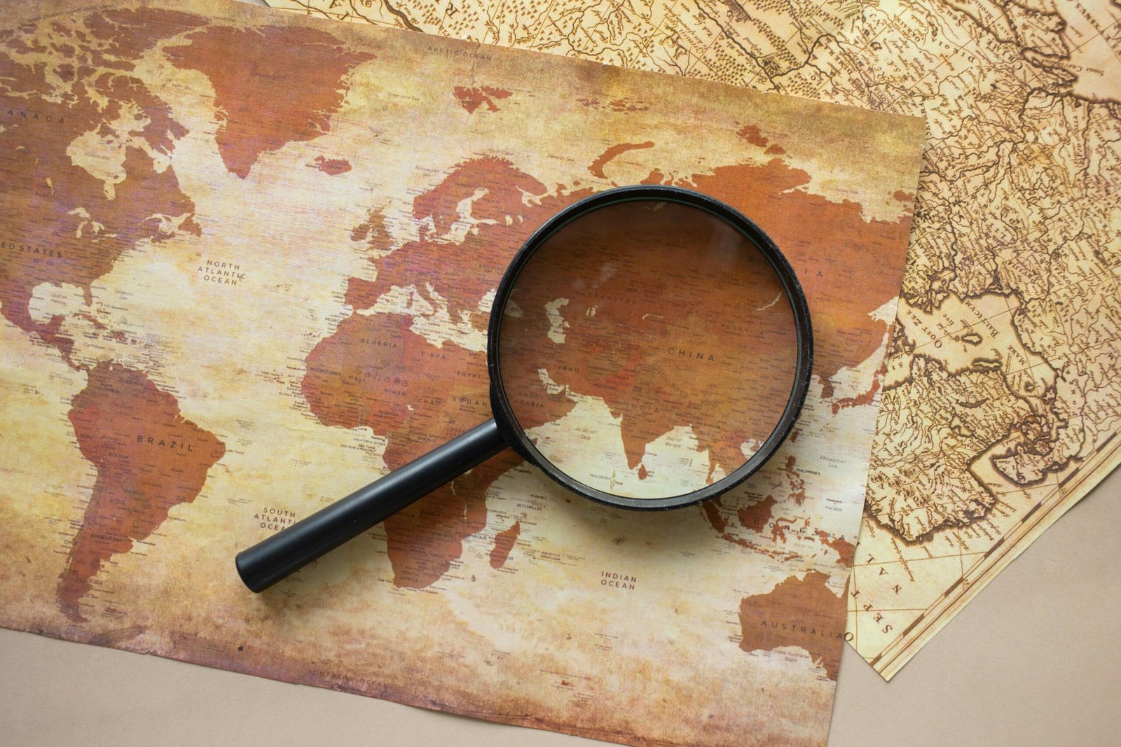 A top view of a vintage world map with a magnifying glass highlighting regions for exploration.
